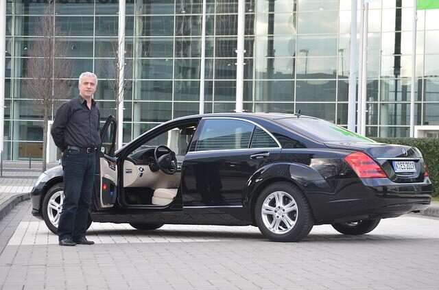 Chauffeur standing on the left door of a luxury car, waiting for the passesnger